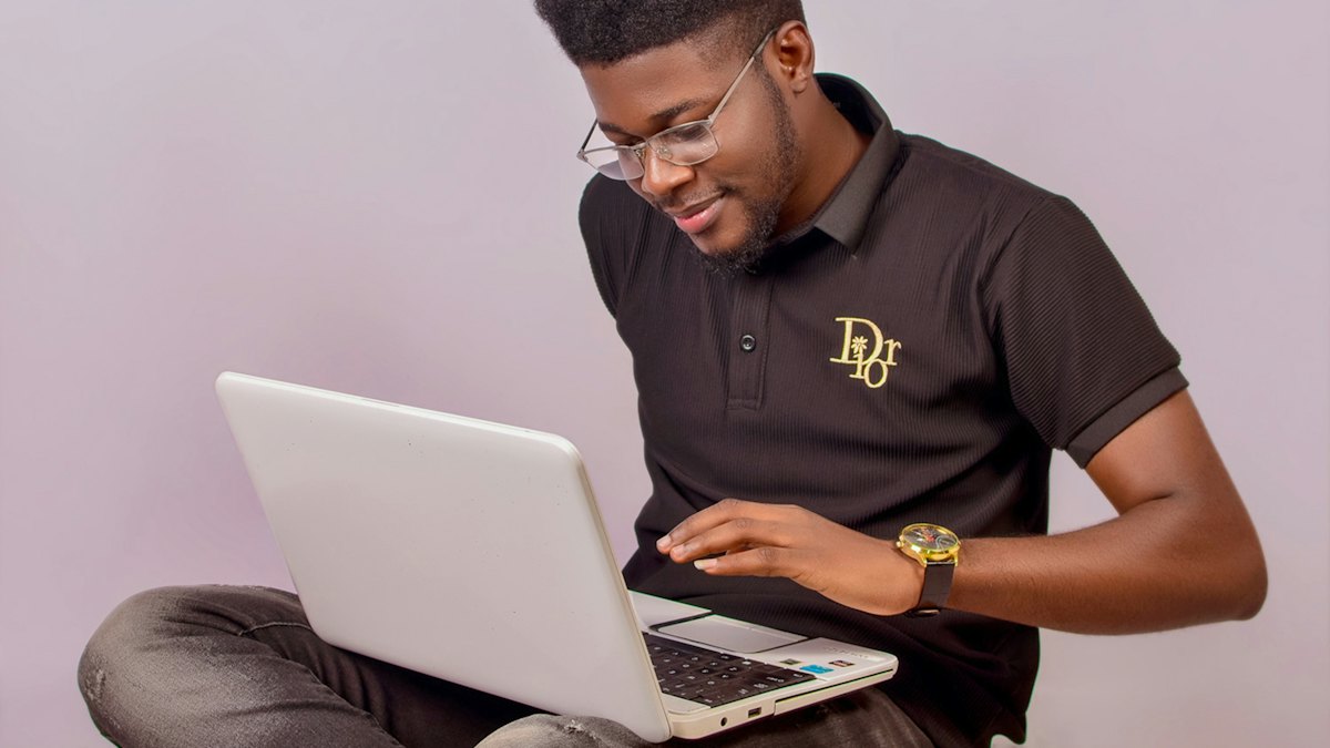 A smiling young man in glasses working on a laptop