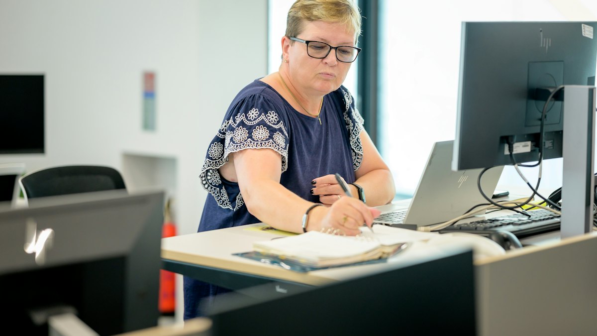 A professional at her desk taking notes beside a computer